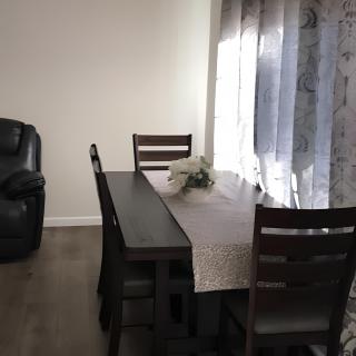 A modern dining room with a dark wooden table, matching chairs, and a window with curtains letting in natural light.