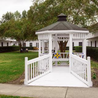 A white gazebo with a walkway in a peaceful park setting surrounded by trees and greenery.