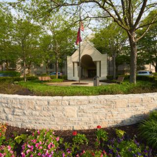 A landscaped garden with a stone wall, colorful flowers, and a small architectural structure surrounded by trees.