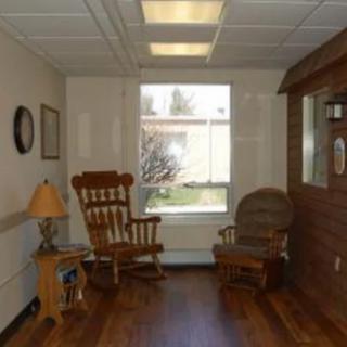 A cozy room with two wooden rocking chairs, a lamp on a side table, and a large window allowing natural light to enter.