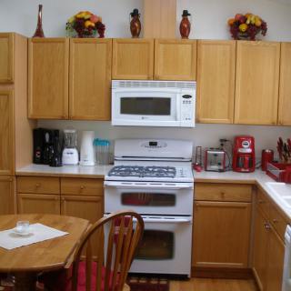 A cozy kitchen with wooden cabinets, a stove and microwave, and various kitchen appliances.