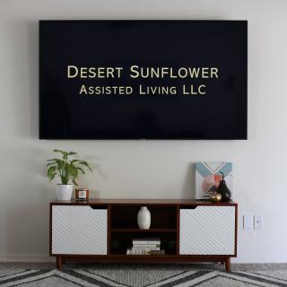 A modern living room setup with a television displaying 'Desert Sunflower Assisted Living LLC' above a stylish cabinet.