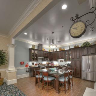 A modern kitchen and dining area featuring wood cabinets, a large clock, and stainless steel appliances.