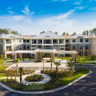 A modern residential building surrounded by a landscaped garden and palm trees on a sunny day.