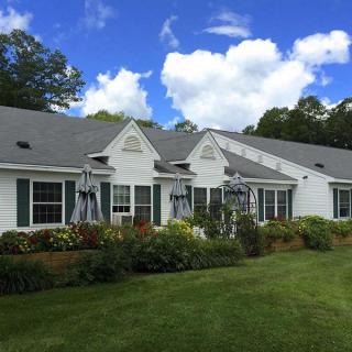 A charming white residential home with a well-maintained garden under a clear blue sky.