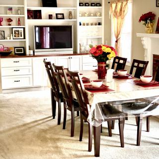 A well-decorated dining room with a large table set for eight, featuring a television and built-in shelves in the background.