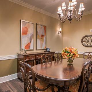 A warmly lit dining room featuring a wooden table, elegant chairs, and decorative wall art.