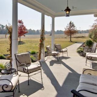 A cozy porch with comfortable seating overlooks a sunny garden landscape.