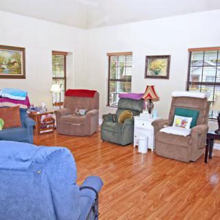 A cozy living room with multiple armchairs and a hardwood floor, adorned with paintings and lamps.