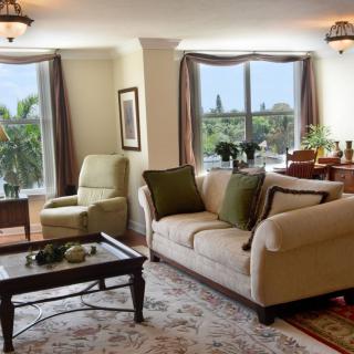 A cozy living room with a sofa and armchair by large windows, featuring a coffee table and elegant decor.