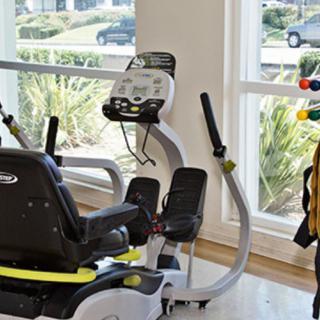 A modern gym featuring a recumbent exercise bike next to large windows overlooking greenery.