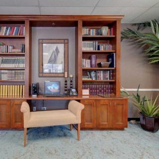 A cozy office space featuring a wooden bookshelf stocked with books and decorative items, alongside a small cushioned bench and indoor plants.