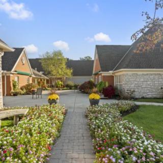 A picturesque garden pathway surrounded by houses, adorned with vibrant flowers under a clear blue sky.
