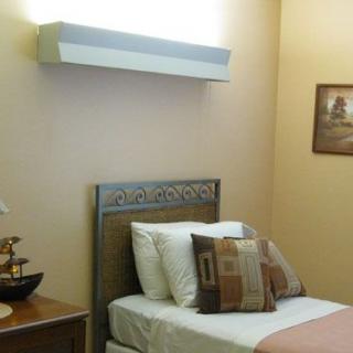 A cozy bedroom with a single bed adorned with decorative pillows, accompanied by a bedside table and lamp, featuring wall art.
