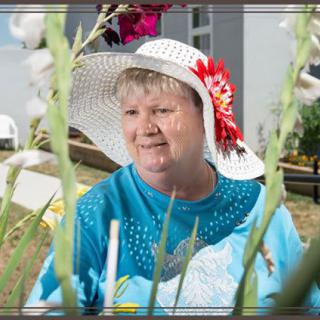 A woman wearing a hat with flowers, sitting outdoors in a garden.
