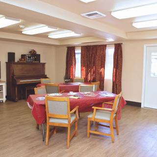 A cozy room with a table and chairs, featuring a piano and red curtains.