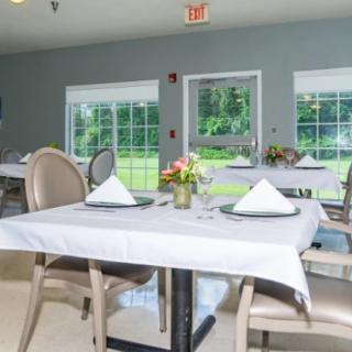 An elegantly set dining room with neatly arranged tables and large windows providing a view of the greenery outside.