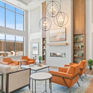 A modern living room featuring high ceilings, large windows, and orange accent chairs around a sleek fireplace.