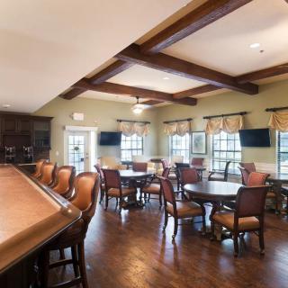 A cozy dining area with wooden furniture and a bar, featuring televisions and large windows.