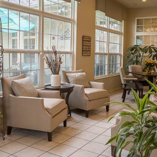 A cozy living area with comfortable chairs, a small table, and lush indoor plants by large windows.