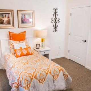 A cozy bedroom with a single bed featuring orange and white bedding, decorative pillows, and elegant wall art.