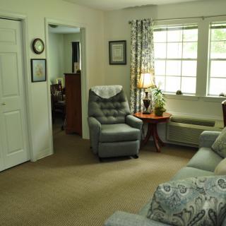A cozy living room with an armchair, sofa, and a lamp next to the window.