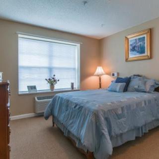 A cozy bedroom with a neatly made bed, a bedside lamp, and a window with blinds.