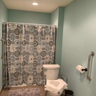 A bathroom with light blue walls featuring a toilet and a shower with a patterned curtain.