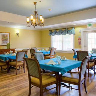A well-lit dining room with tables set for meals, featuring elegant chandeliers and blue tablecloths.