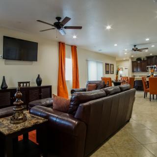A modern living room with a cozy arrangement featuring a large couch, ceiling fans, and bright orange curtains.