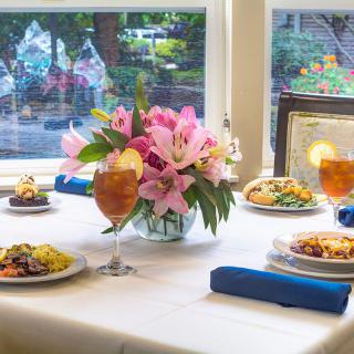 A beautifully set dining table with floral centerpiece, various dishes, and iced tea by a window.