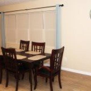 A dining room with a wooden table and four chairs, featuring placemats and a window with curtains.