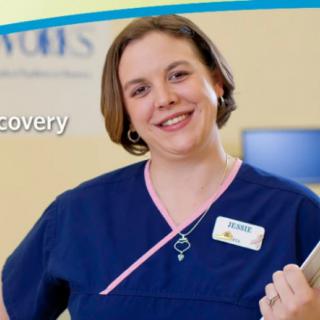 A smiling nurse in a blue uniform holding a clipboard.