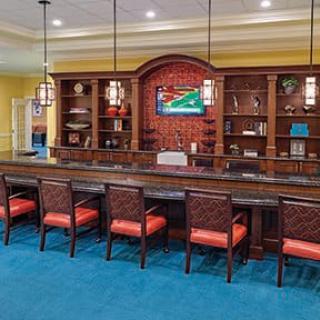 A modern lounge area with a bar-style seating arrangement, featuring bookshelves and pendant lighting.