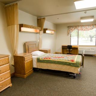 A clean and orderly hospital room with a single bed and wooden furniture.