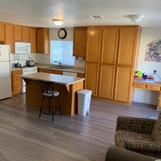 A cozy kitchen with wooden cabinets and a small island, adjacent to a living area.