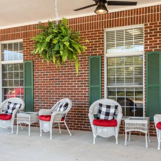 A cozy porch with wicker chairs, checkered cushions, and a hanging plant against a brick wall backdrop.