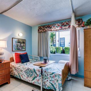 A cozy hospital room with a single bed, floral bedding, and a large window allowing natural light.