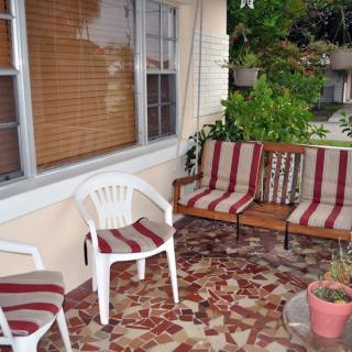 A cozy patio with a swing bench and plastic chair, both featuring striped cushions.