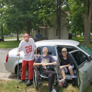 A group of friends enjoying a sunny day outside with a car and wheelchair.