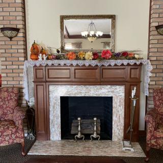 A cozy indoor fireplace with autumn decorations on the mantel, flanked by two armchairs.