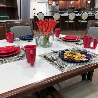 A dining table set with red and blue dinnerware, featuring a centerpiece of orange flowers.