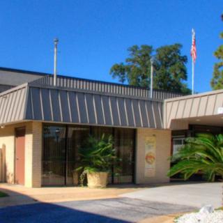 The exterior view of a building with a prominent entrance, featuring flags and potted plants.