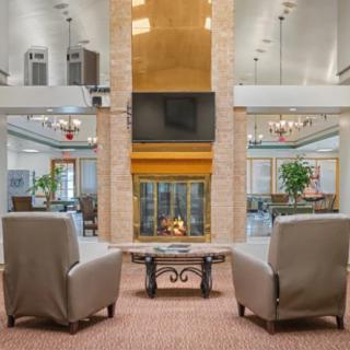 A cozy lobby featuring a central fireplace with comfortable chairs arranged symmetrically around it.