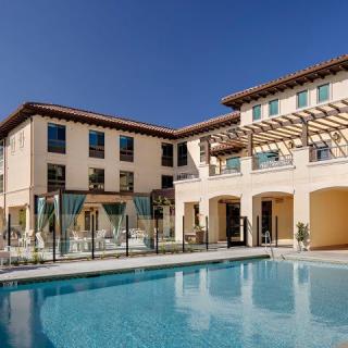A luxurious residential building with a large outdoor swimming pool on a sunny day.