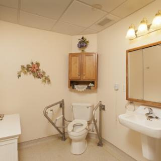 An accessible bathroom featuring a toilet, sink, and safety handrails.