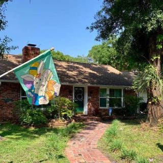 A brick house with a flag in the front yard, surrounded by greenery and trees on a sunny day.
