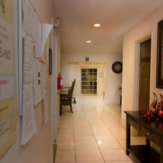 A well-lit hallway with a view of a kitchen area, featuring a table and bulletin board.