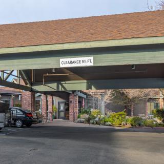 A hotel entrance with a car parked under the canopy and a clearance sign.