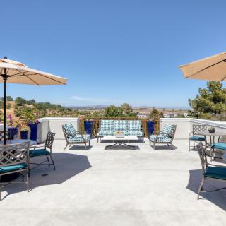 A spacious outdoor patio with seating arrangements and umbrellas, offering a scenic view of the skyline.